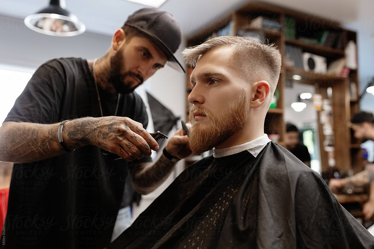 Barber trimming beard of handsome young man