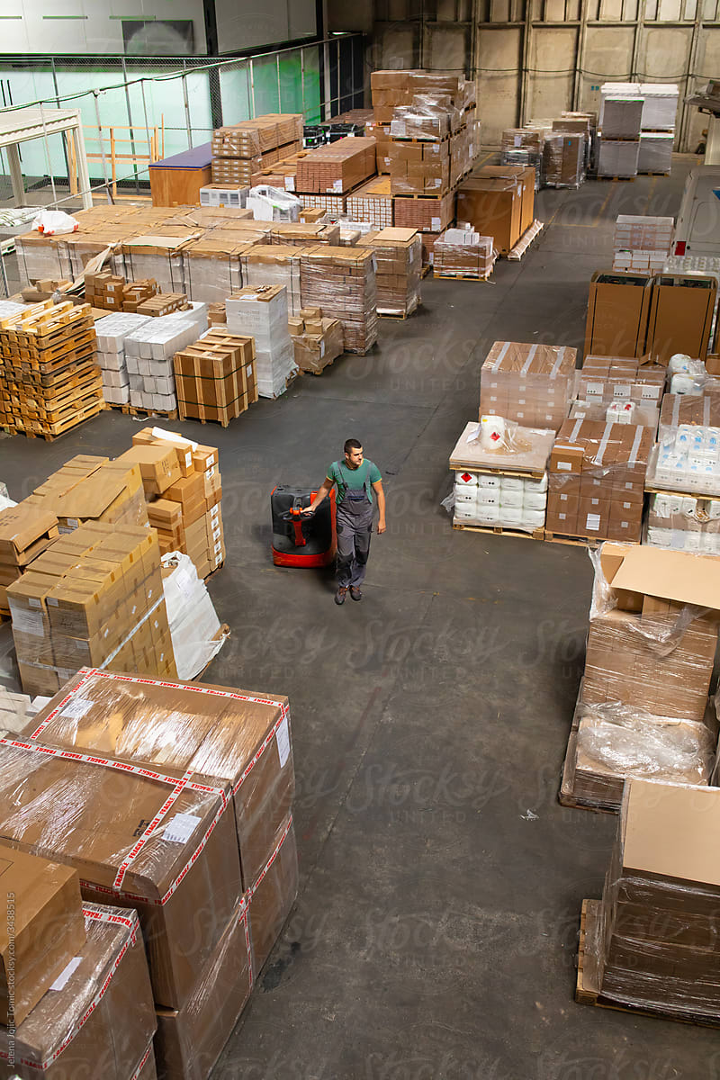 One man operates the pallet jack in a warehouse full of shipping goods