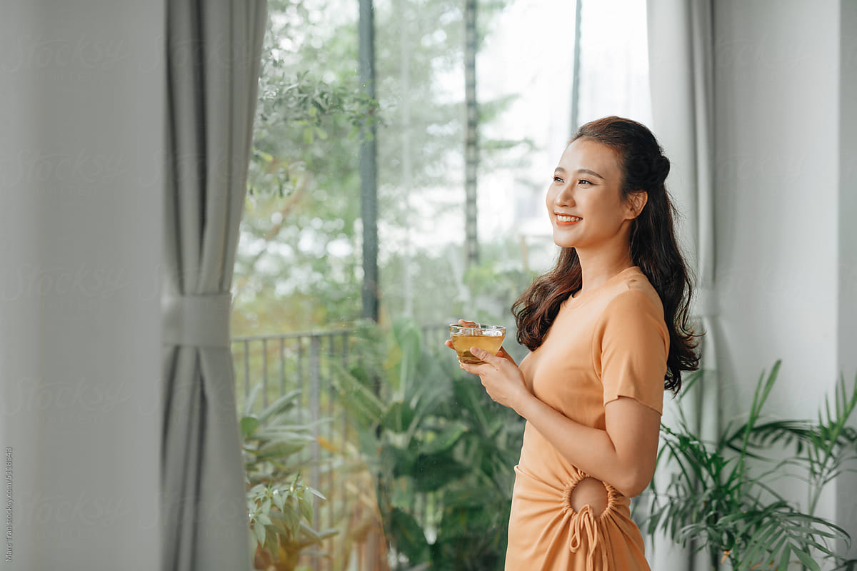 positive asian lady enjoying morning tea in cozy living room