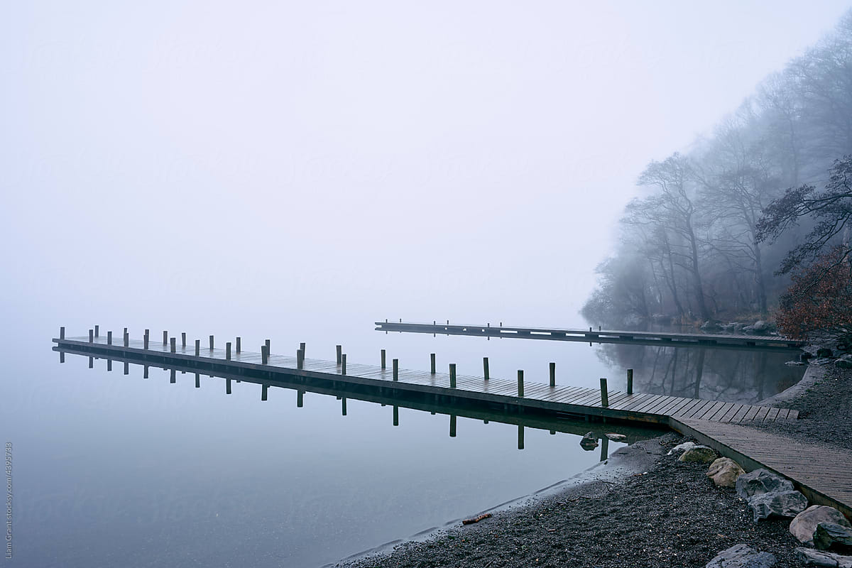 Jetty and trees on Lake Windermere in fog at dawn