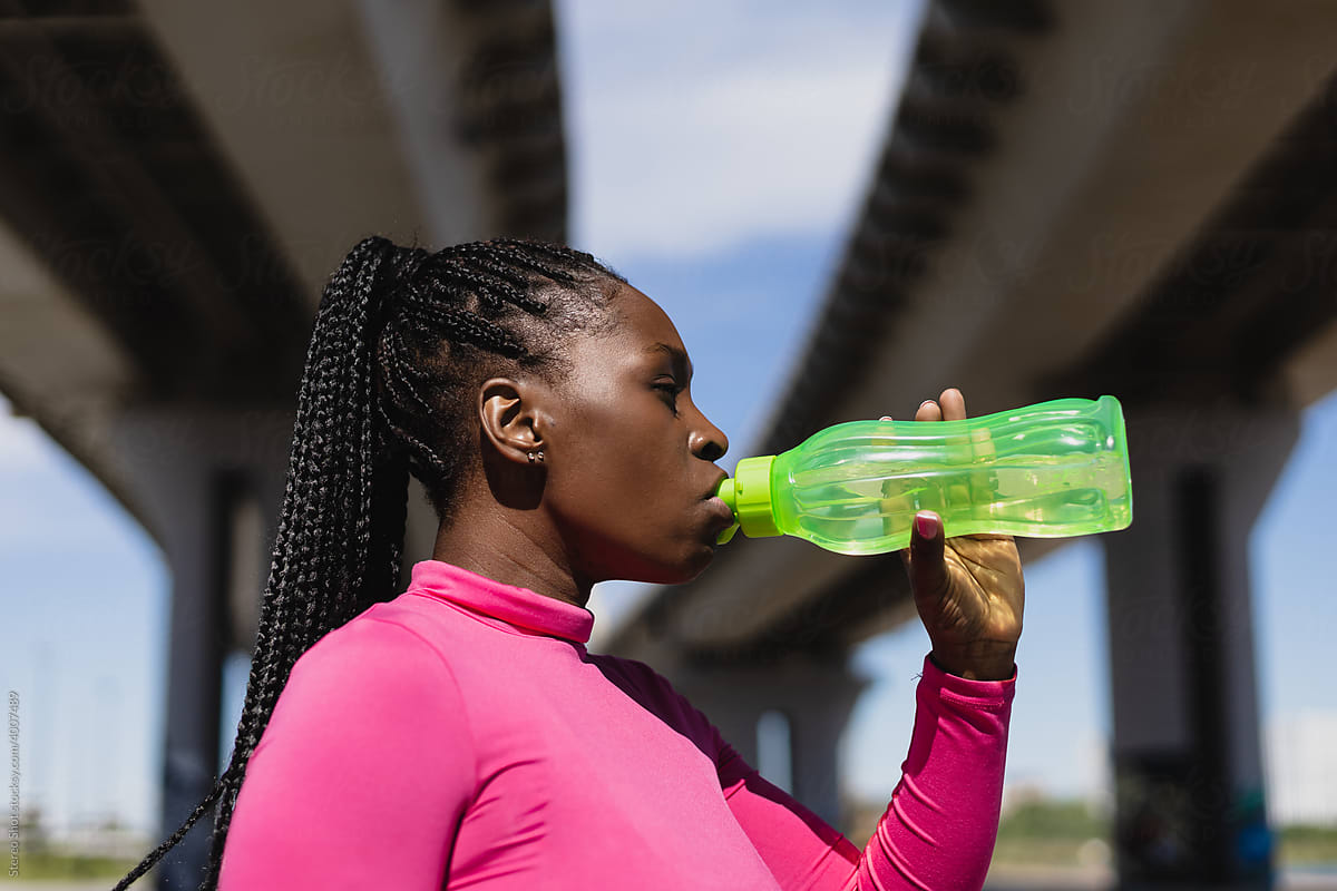 Black athletic woman drinking water during workout