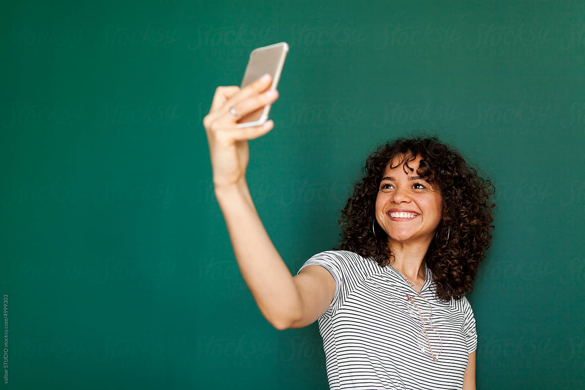 Cheerful woman taking selfies front green wall