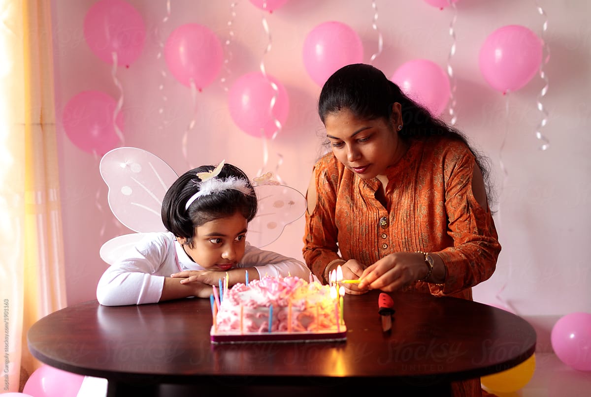 Mother lighting the candles on the birthday cake and her daughter watching