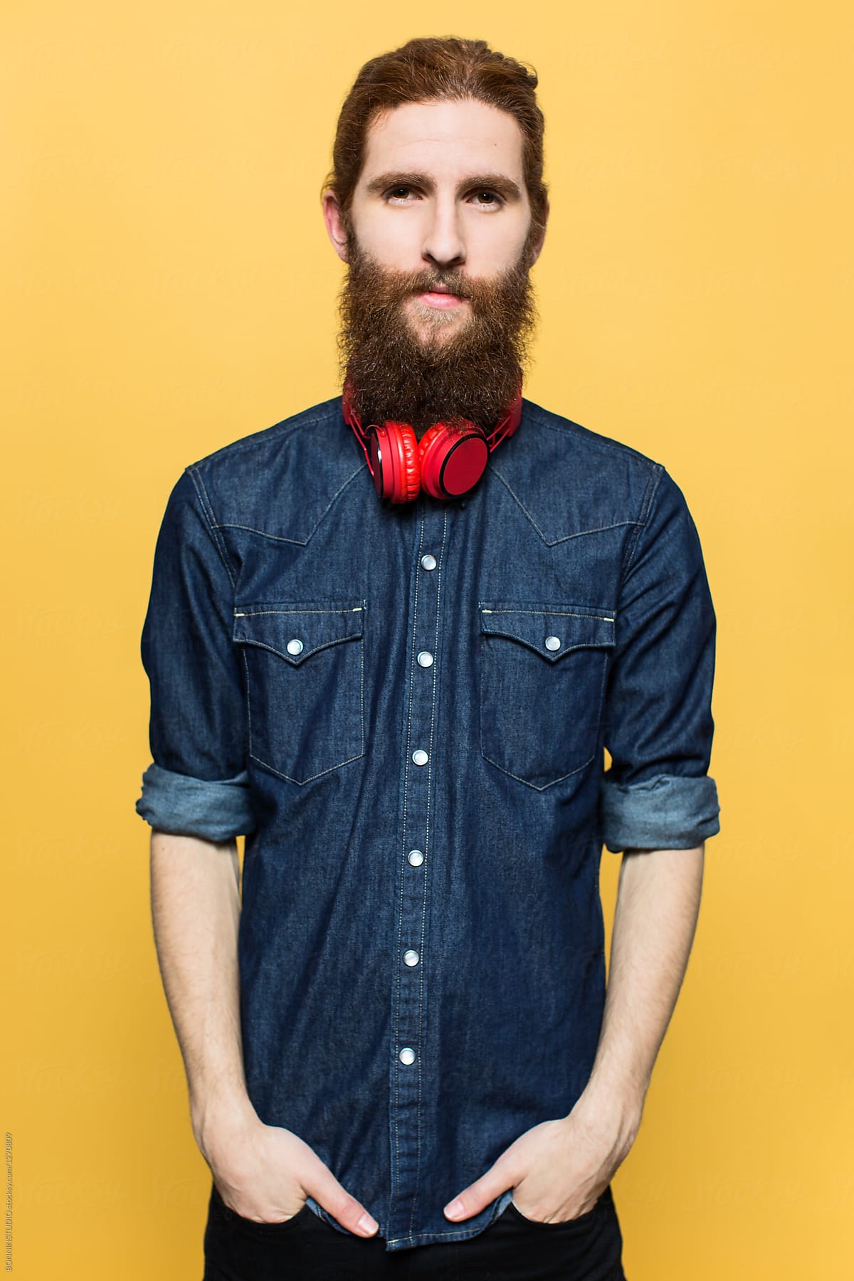 Portrait of a bearded man wearing red headphones in front a yellow wall.