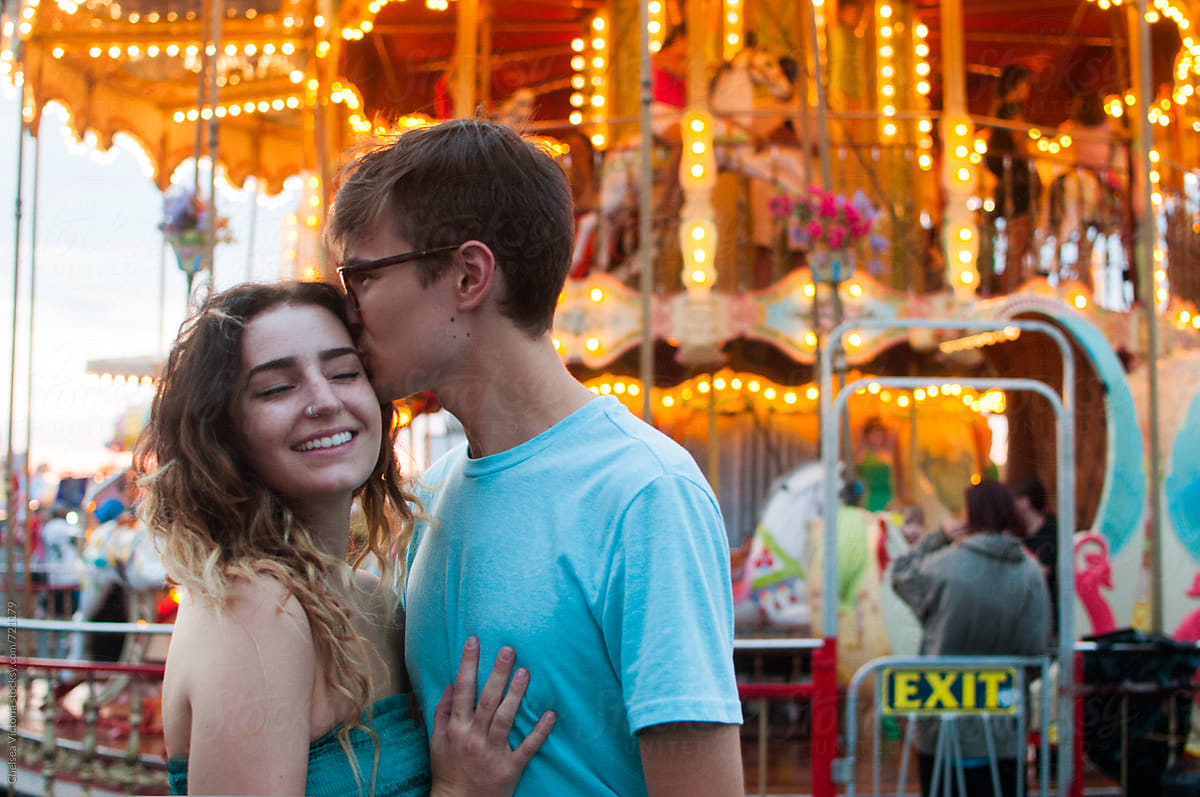 A couple kissing in front of a carousel