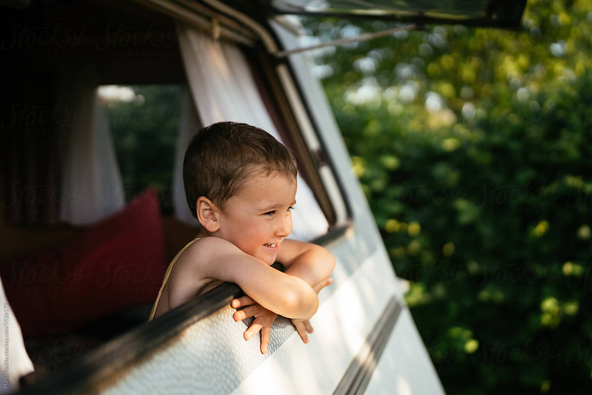 Cute smiling kid sitting in van near window in daylight