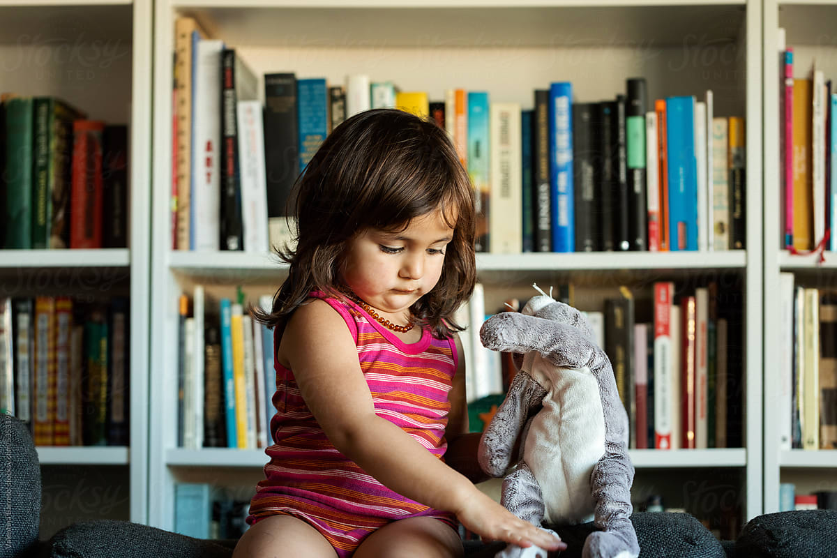 Girl playing with stuffed rabbit sitting on couch