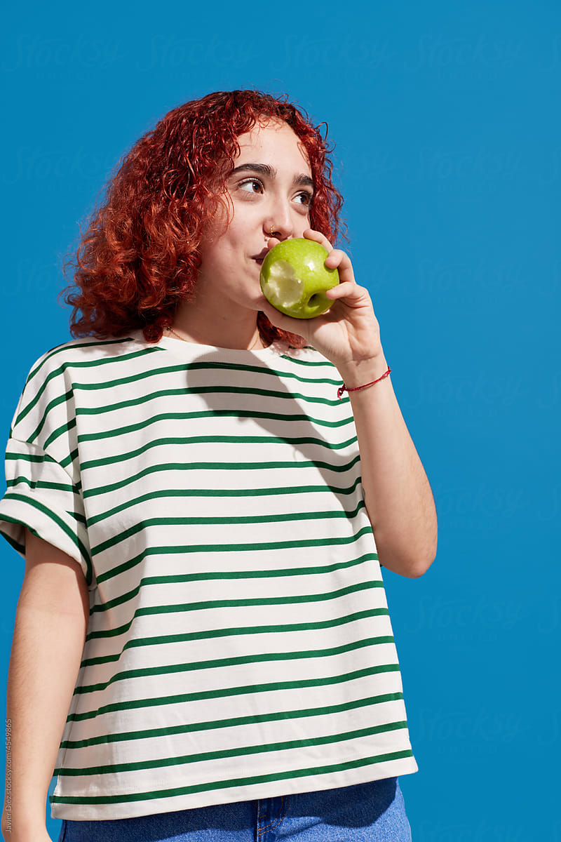 Redhead woman biting fresh apple in studio