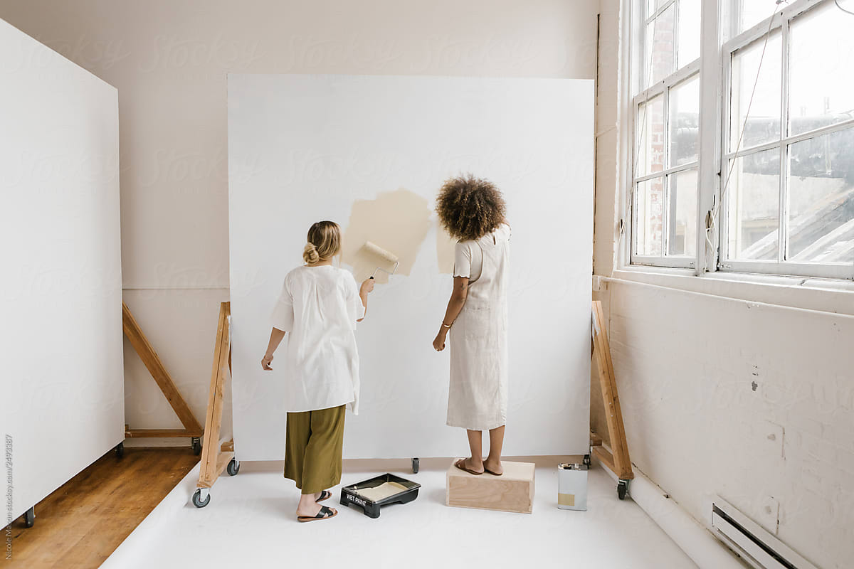 two young women painting a backdrop wall in bright room