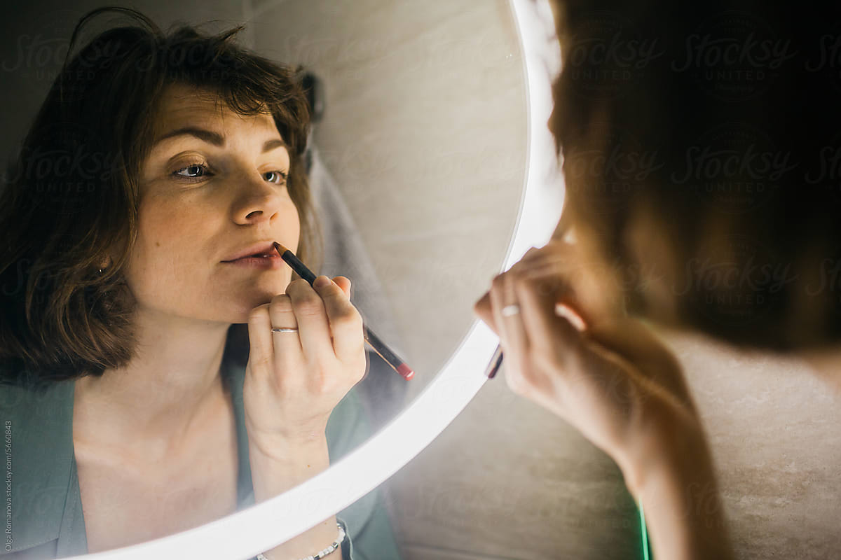Young woman putting on makeup in front of the mirror