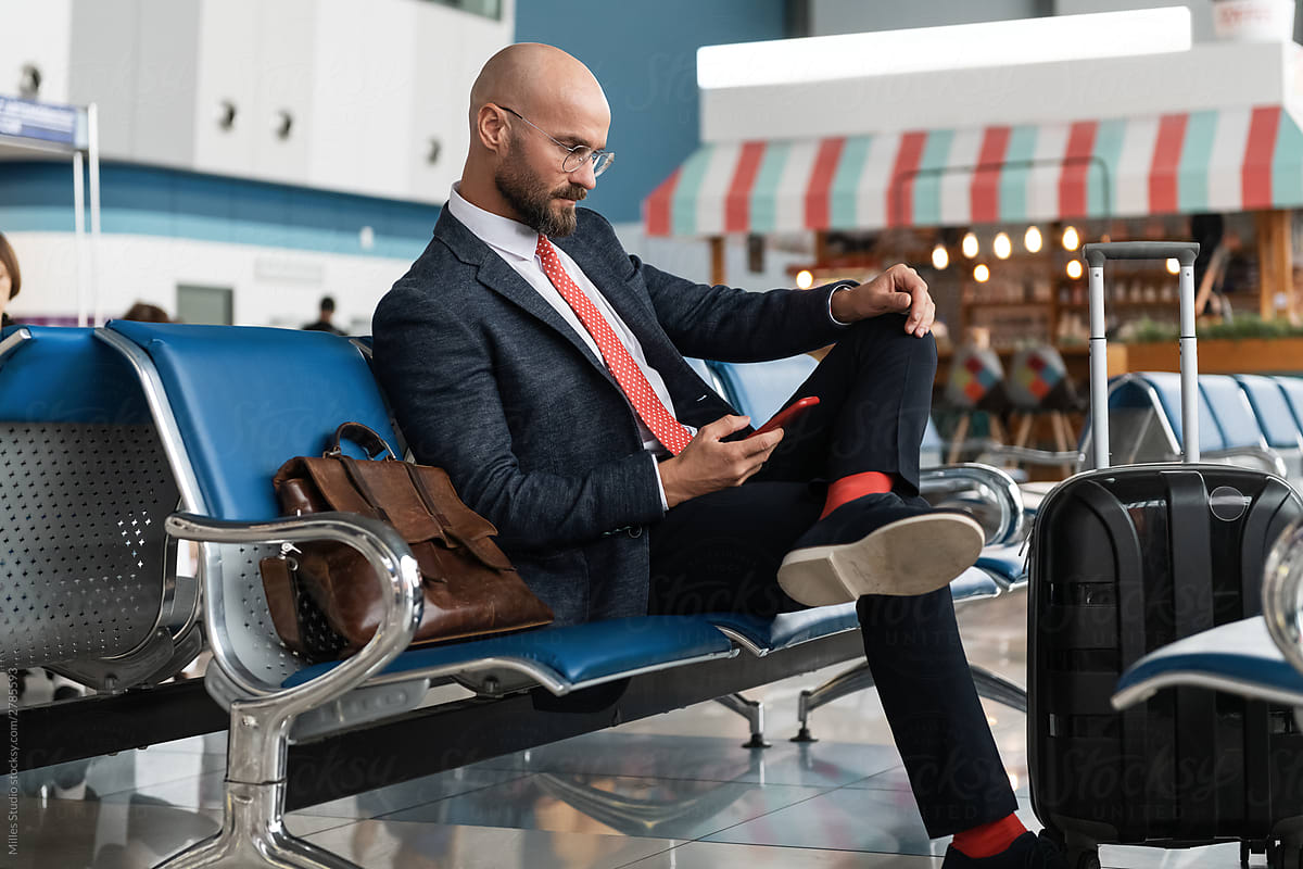 Bearded manager using smartphone in lounge room of airport