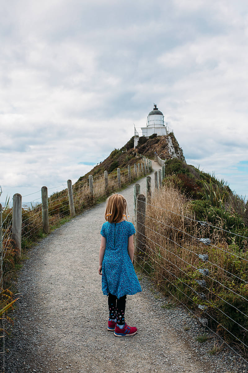 Young girl walking on a path towards a lighthouse