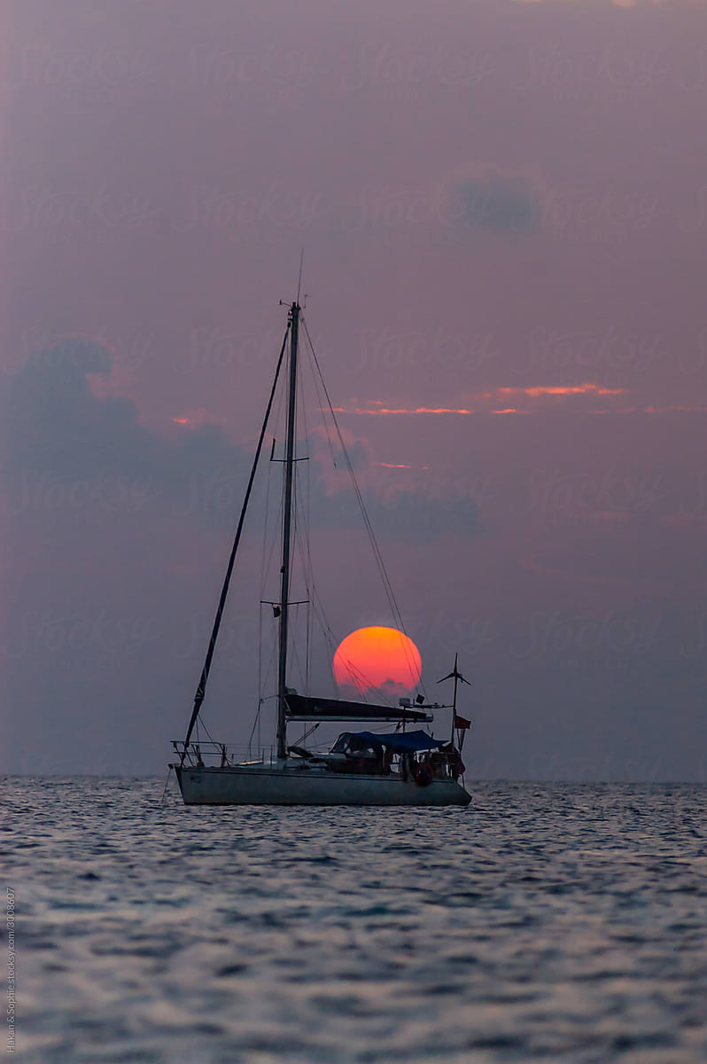 the sun is setting over a sailboat