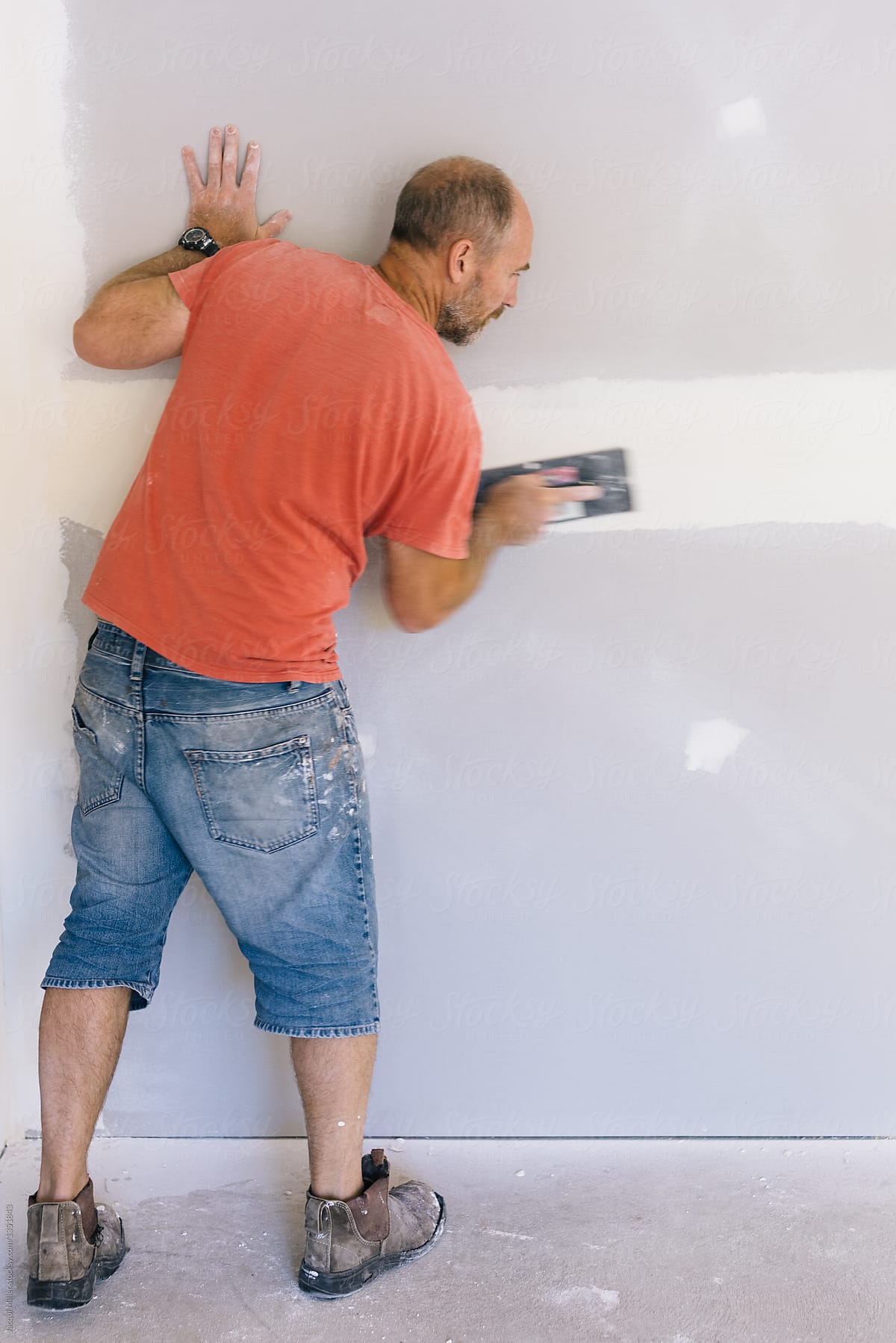 Home handyman sanding plasterboard wall - vertical