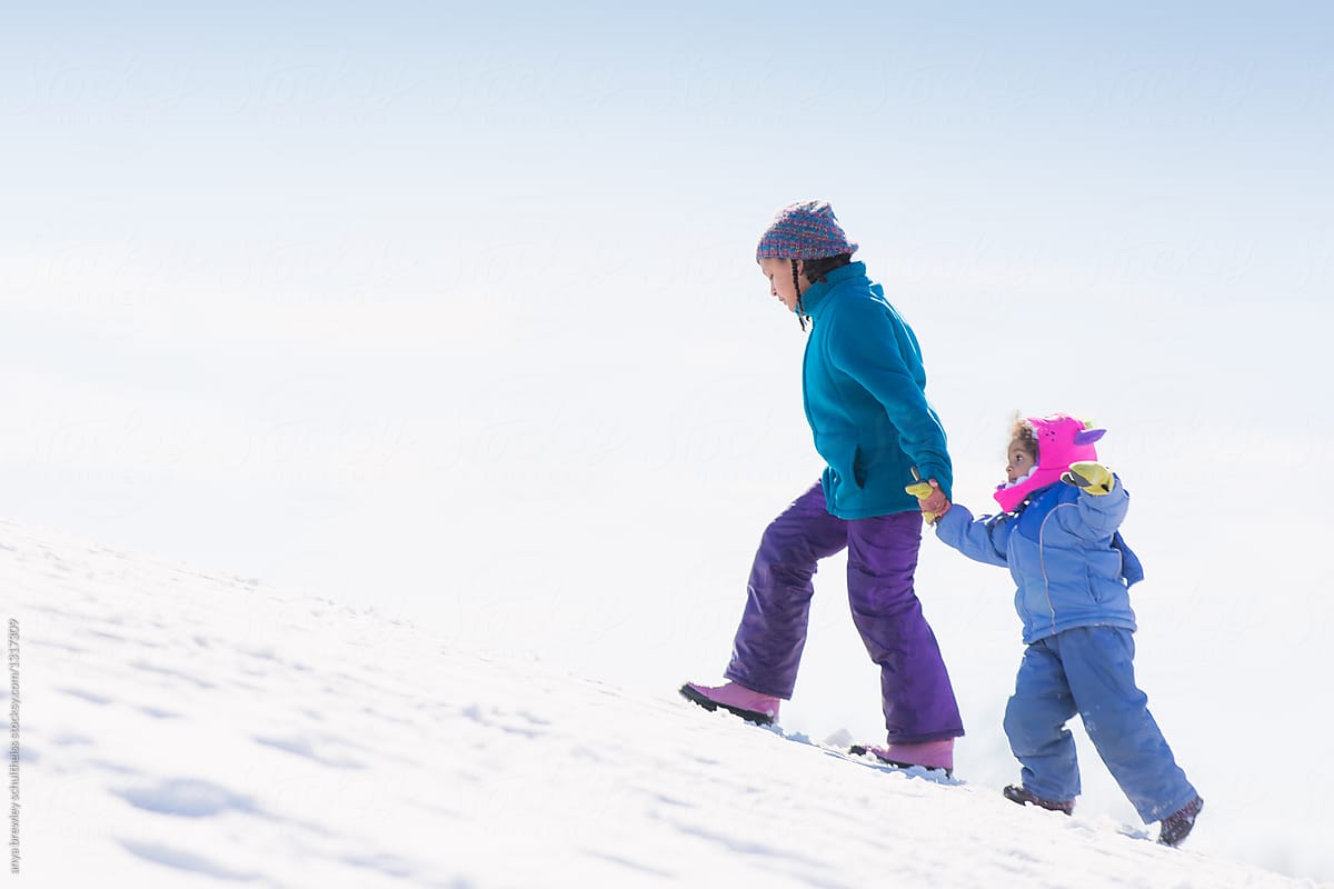 A young girl helping her sister walk up a snowy hill