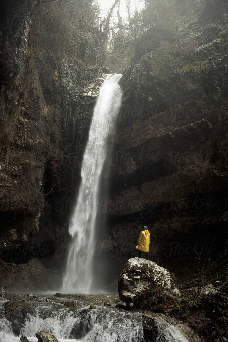 Man in a yellow raincoat standing on a hill  and looking to the waterfall
