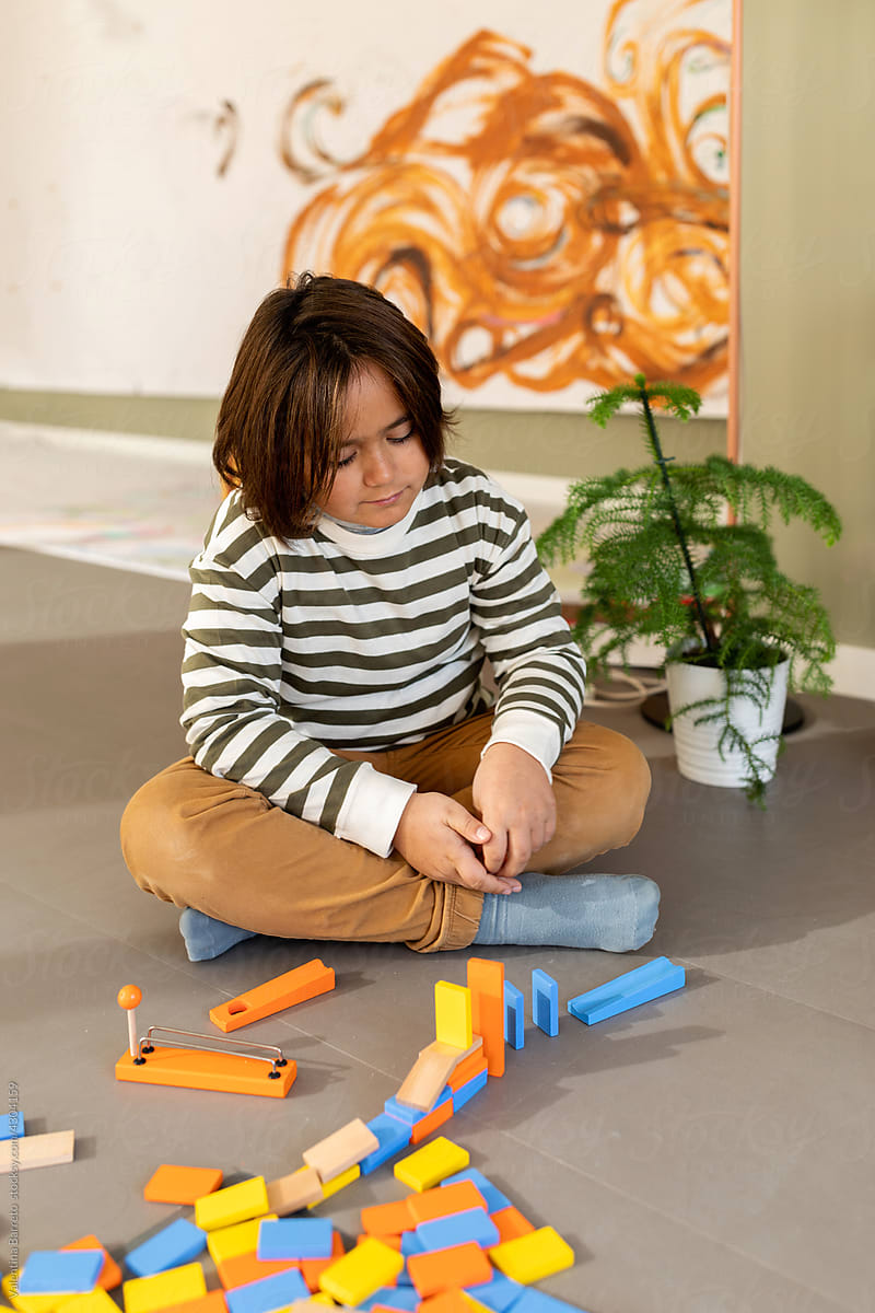 Boy playing with wooden dominoes sitting on the floor