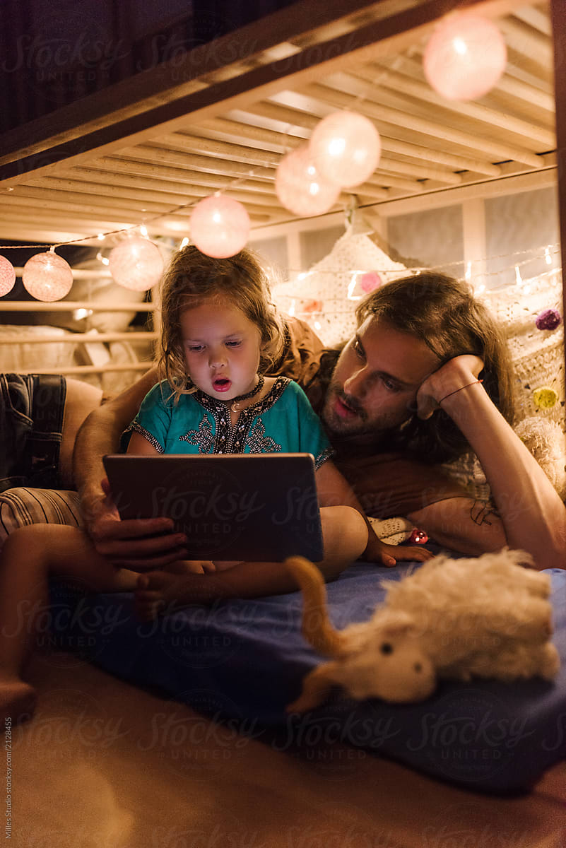 Girl with father watching tablet on bed