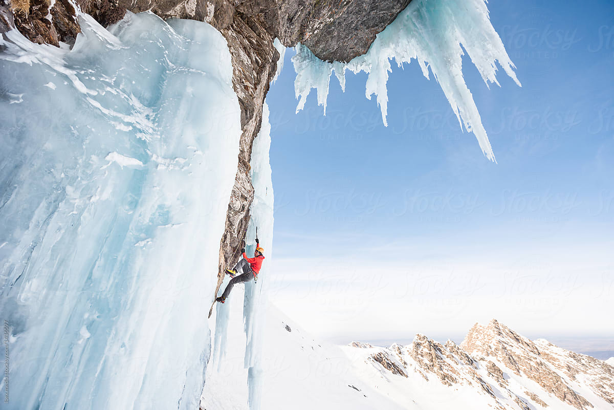 Alpinist holding on ice axes while ascending on frozen waterfall