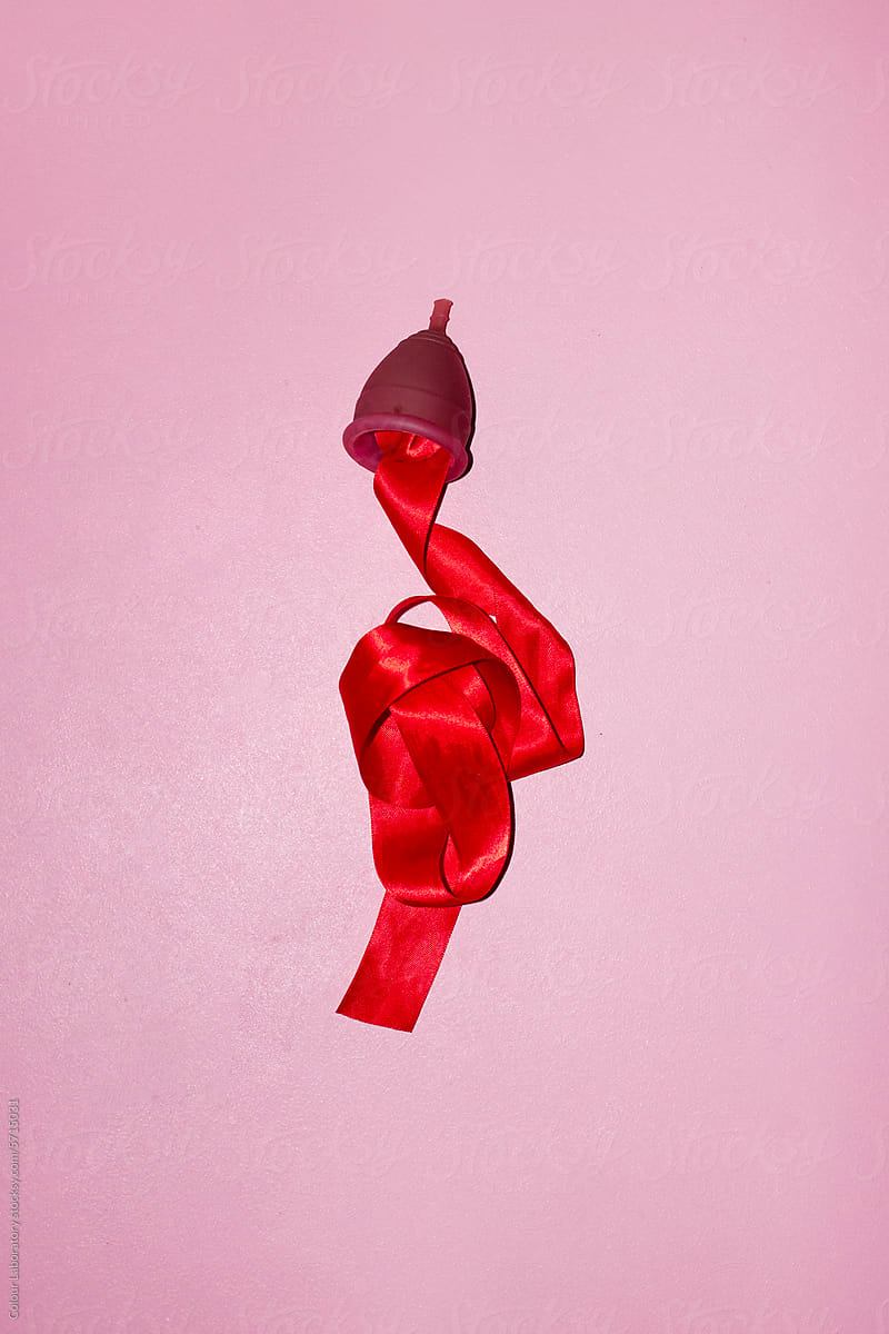 Conceptual photo of period / menstrual cup & red silk ribbon as blood
