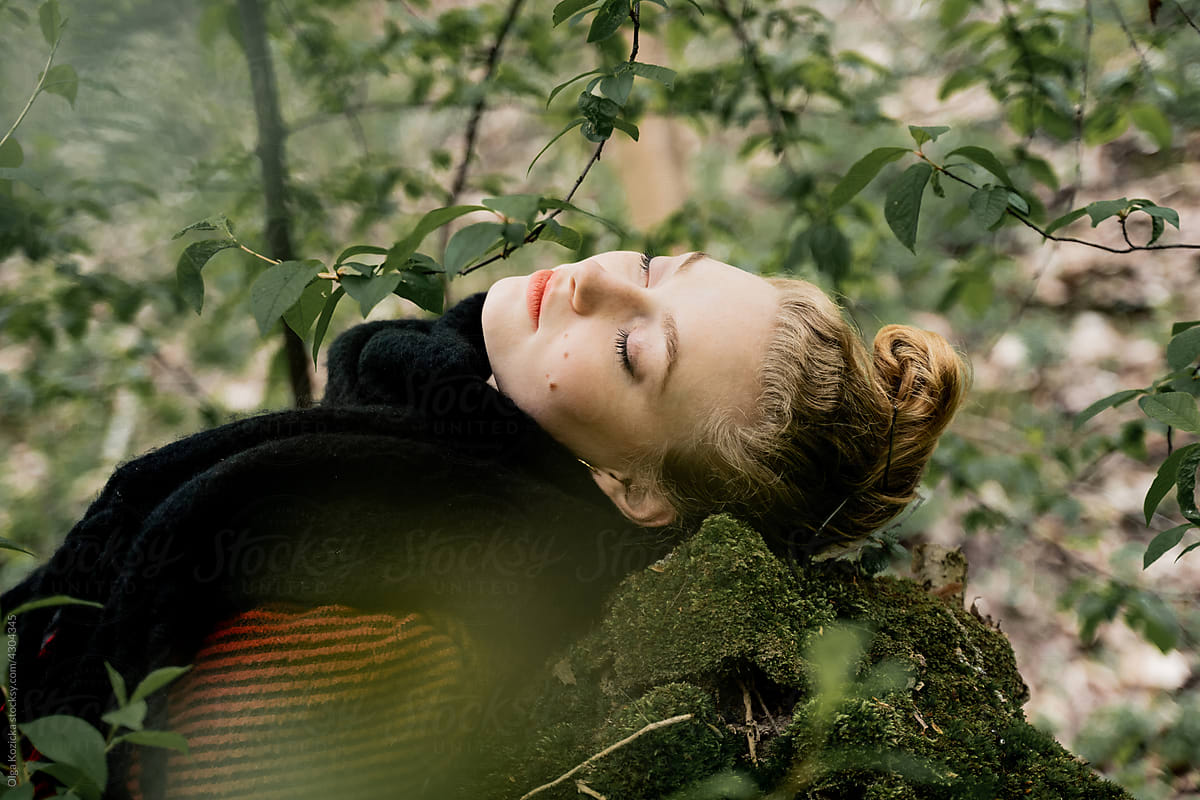 Blonde Woman With Closed Eyes Lying On Rock In Forest