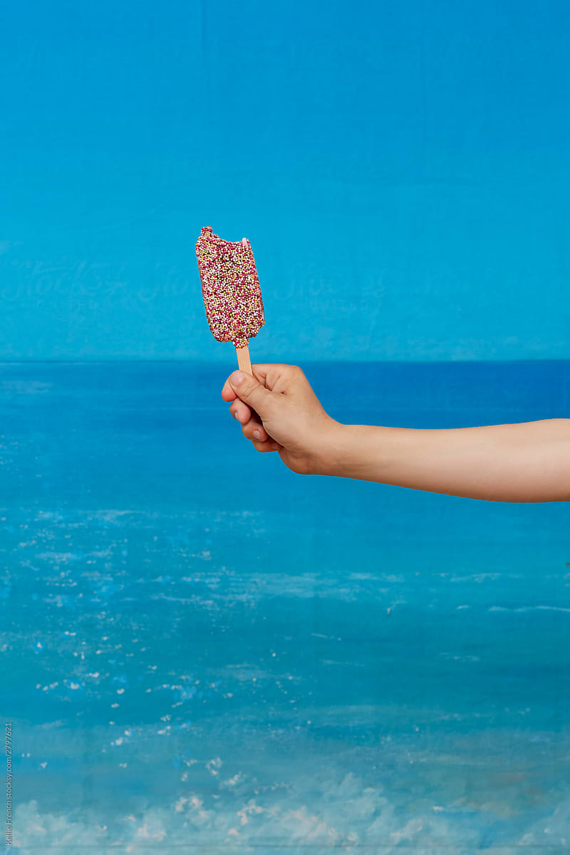 Child holds nobbly bobbly lollipop against a painted background of sea on a beach