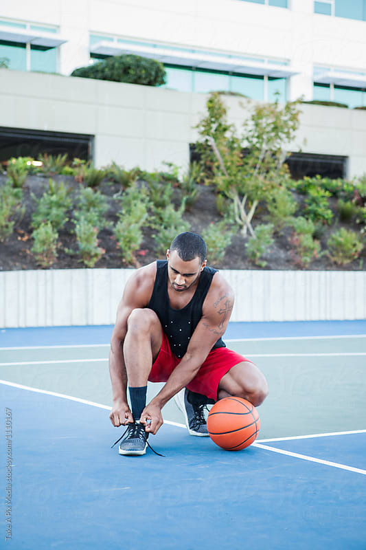African American man tying up his shoes on an outdoor basketball