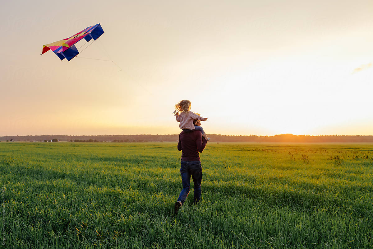 Father and kid having fun with kite in field