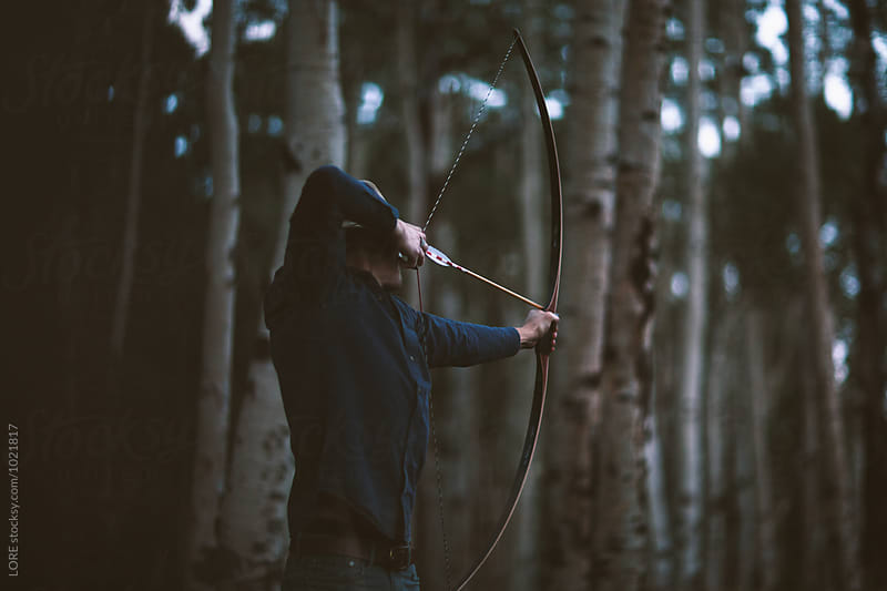 Adult male archer shoots a bow and arrow in aspen forest
