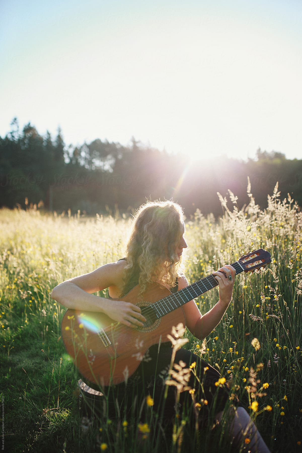 Young woman sitting in field at sunrise playing classical guitar and singing