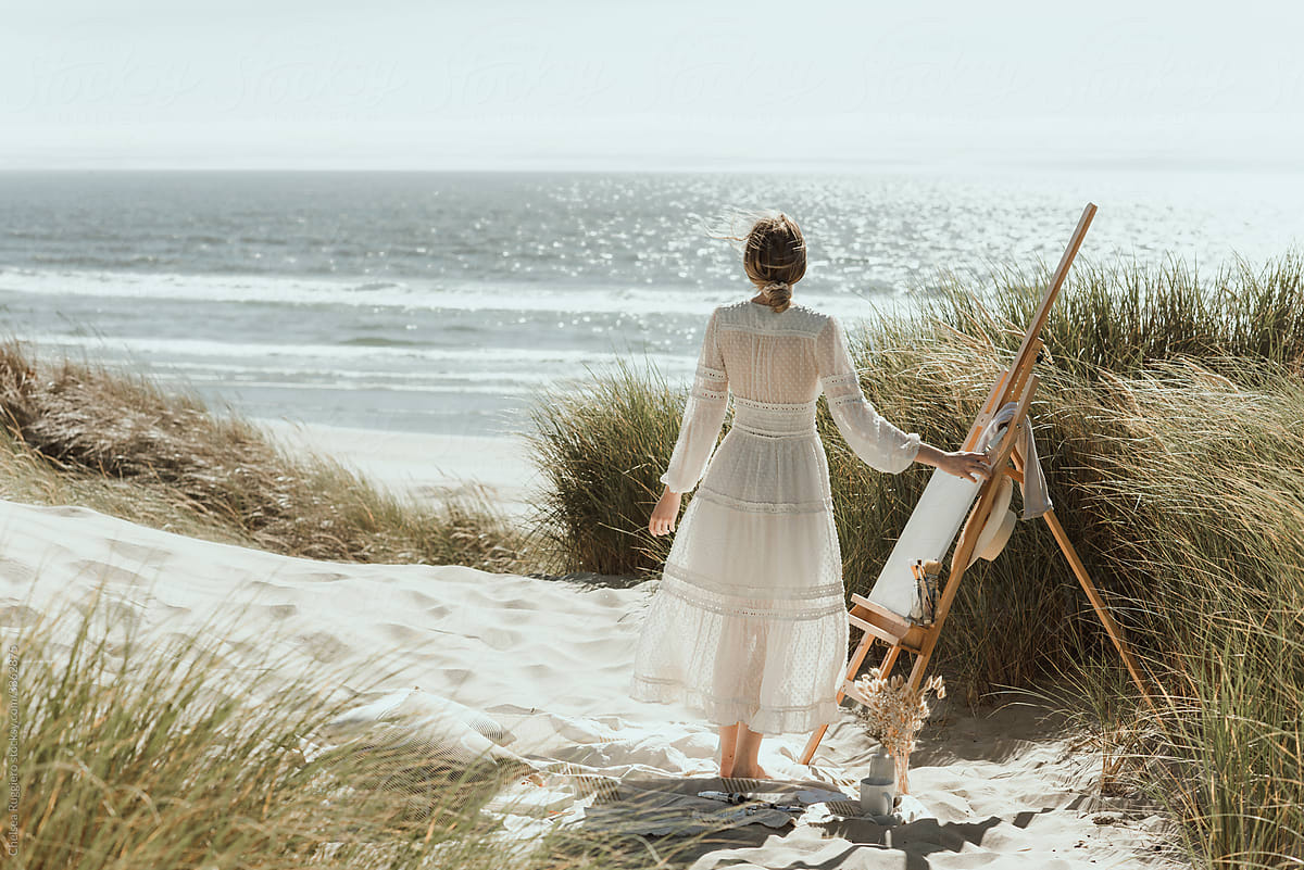 Young woman painting on an easel at the coast in the dunes