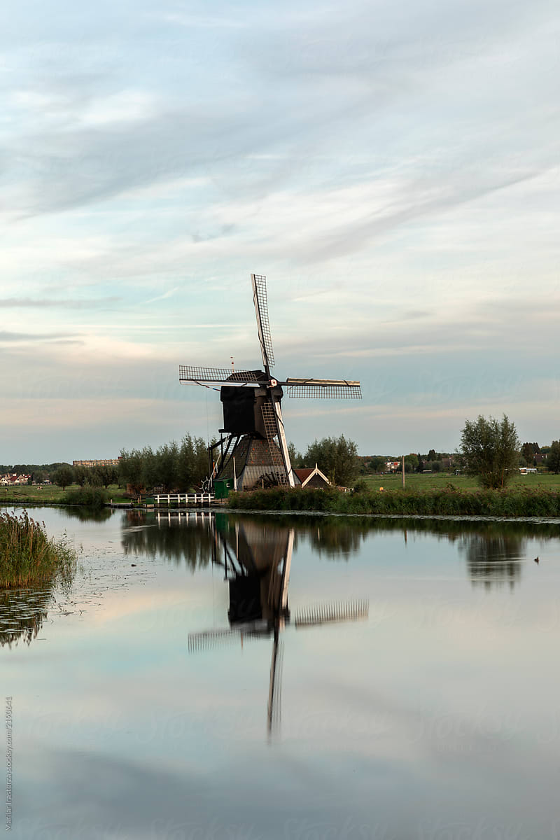 Scenic sunset landscape with windmill, blue sky and reflection in the water