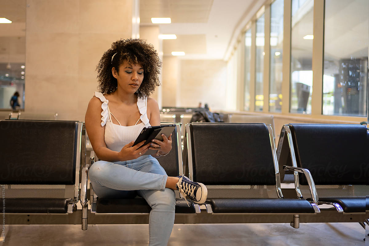 Black traveler with tablet sitting on bench in airport