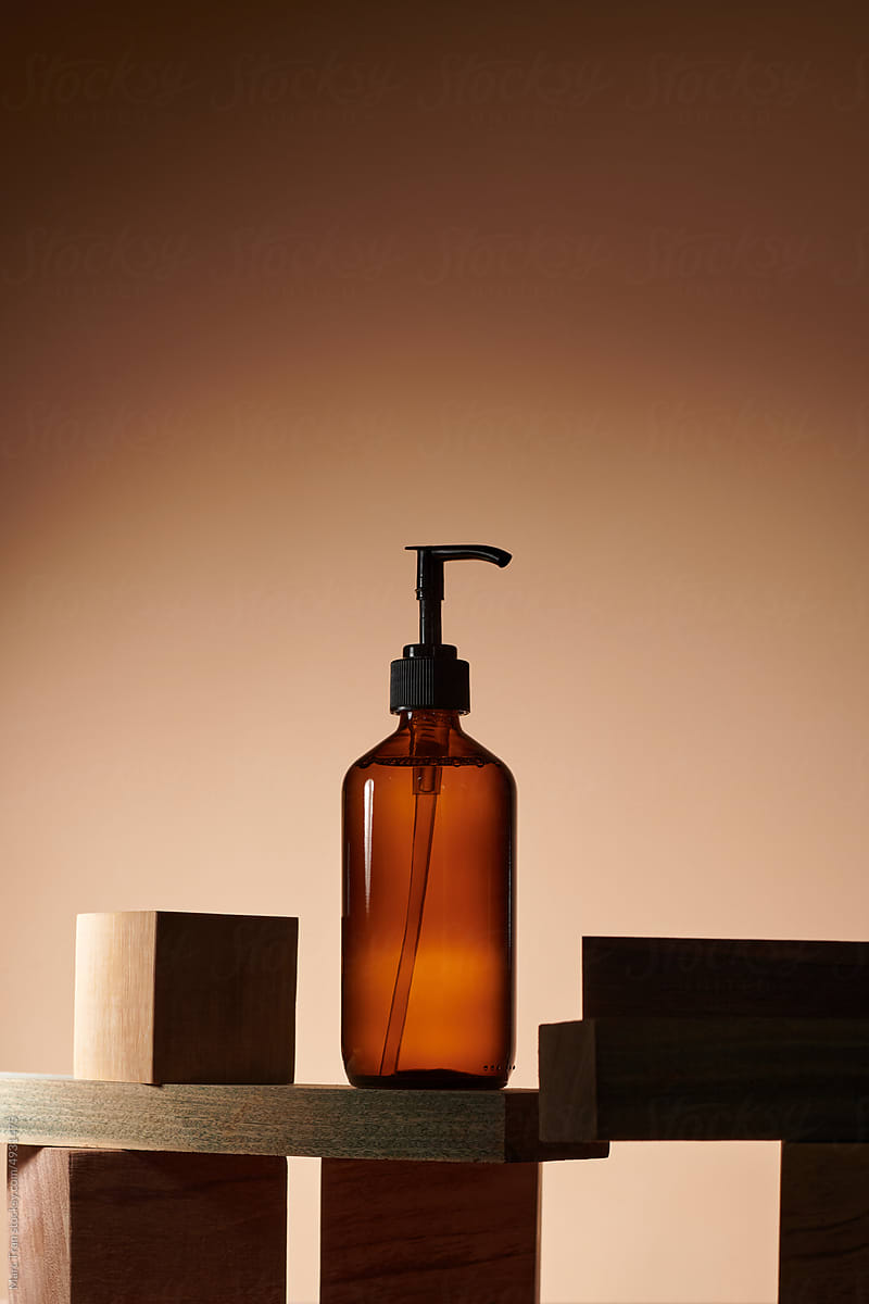 Dark amber glass pump bottle on the wooden cut podium with back light