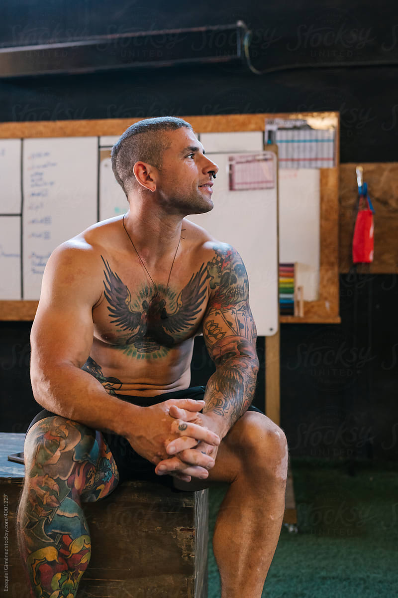 Tattooed sportsman sitting on cube and resting