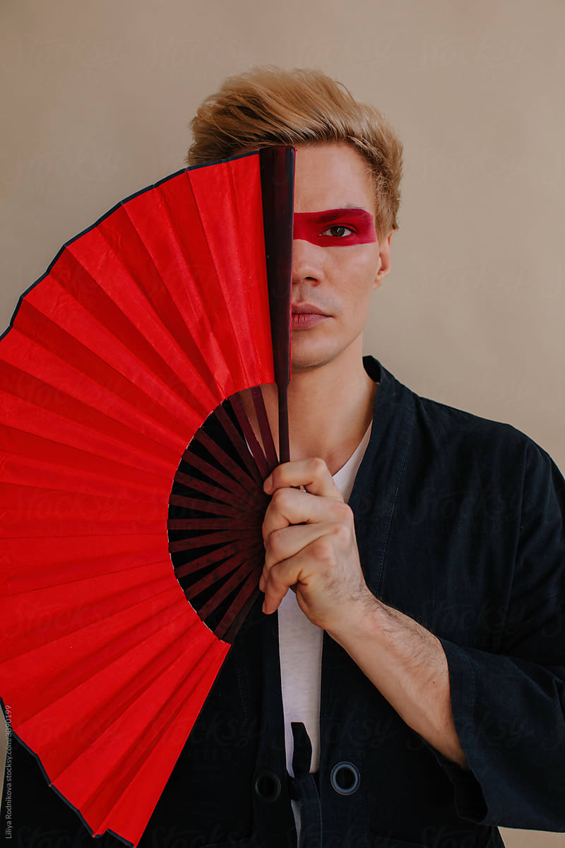 Male model covering painted face with hand fan