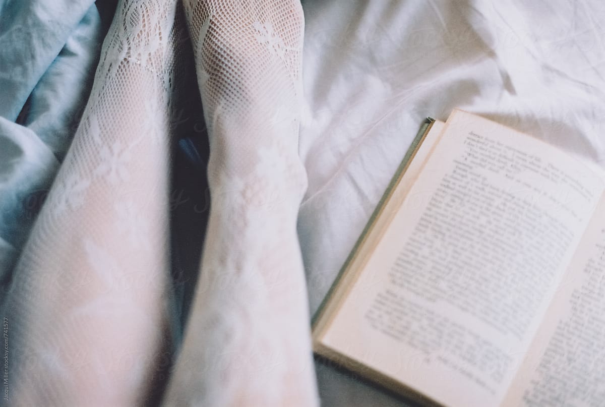 Woman\'s legs, in stockings, on bed with open book