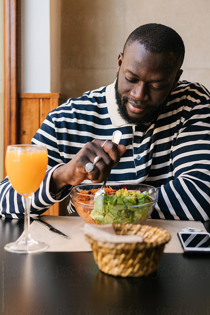 Black man eating a salad inside a restaurant.