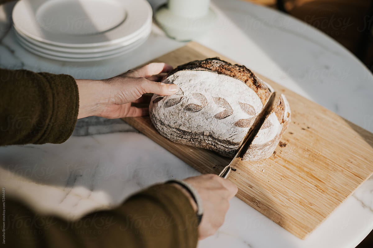 Hands cutting a loaf of fresh sourdough bread.
