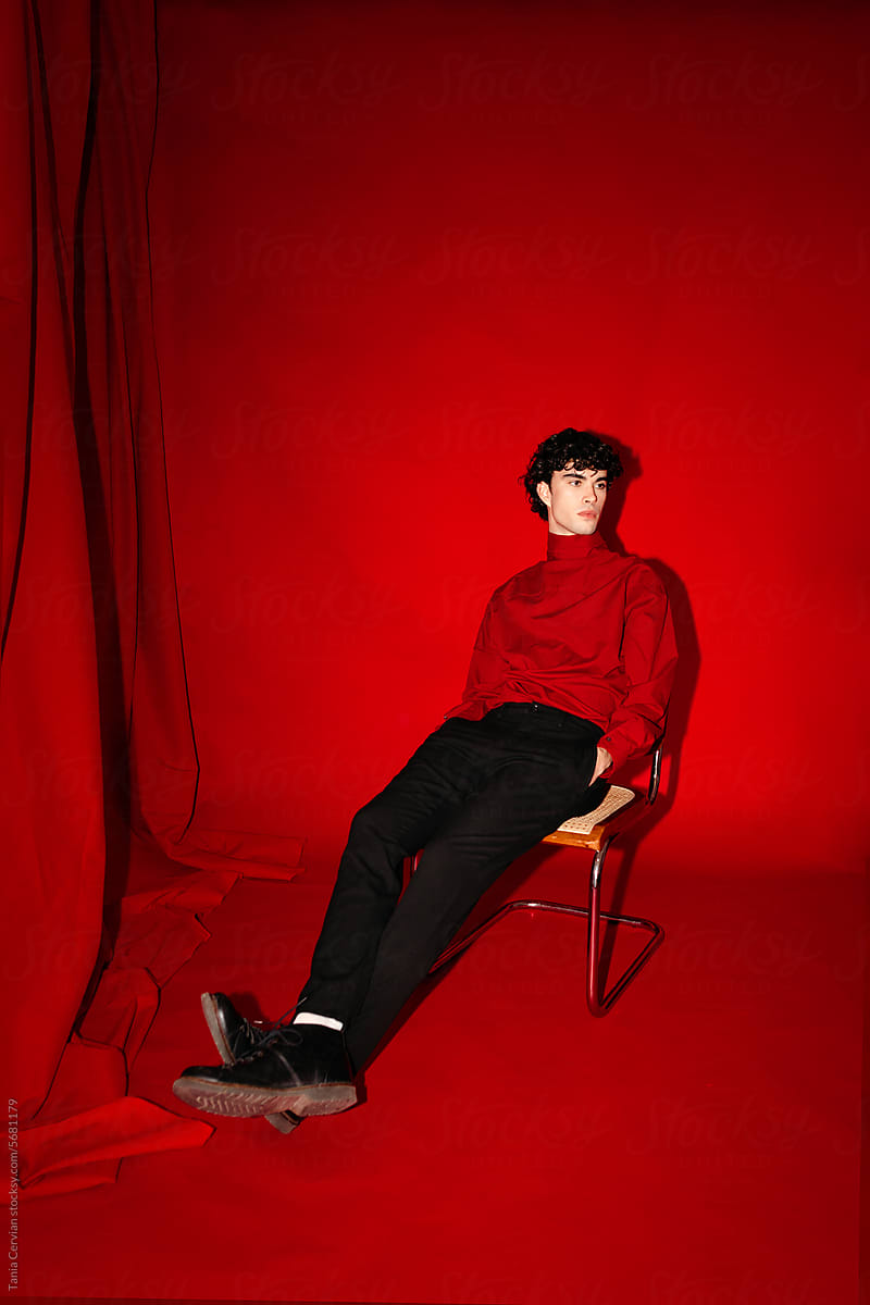 Stylish young man sitting on chair near red backdrop