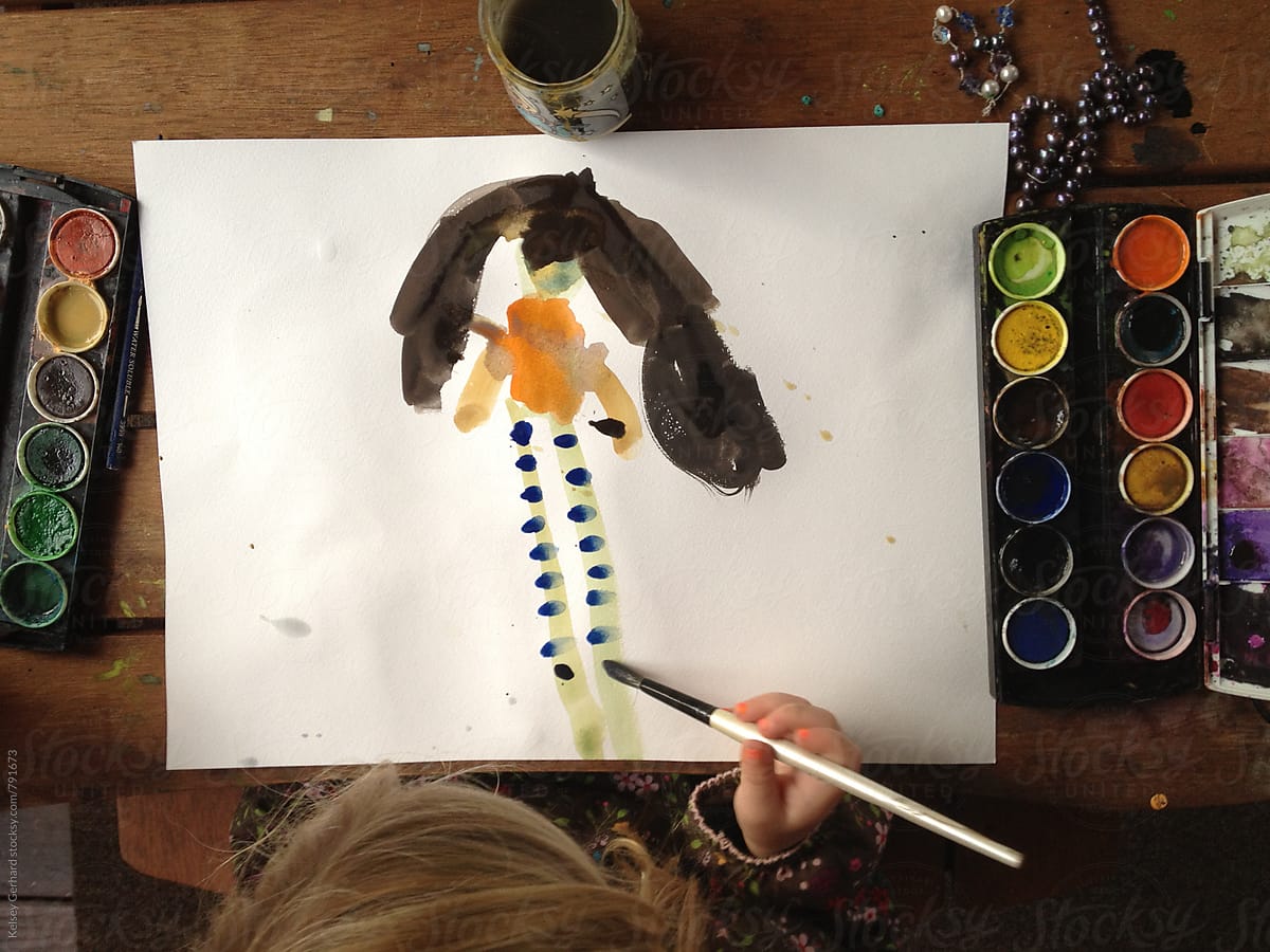 A shot from above of a young girl painting with watercolors.