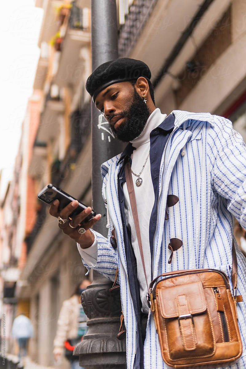 Confident black guy using phone at street lamp