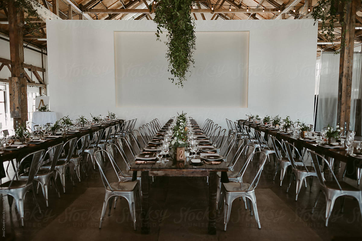 Long harvest tables with simple greenery and copper details in industrial setting for wedding