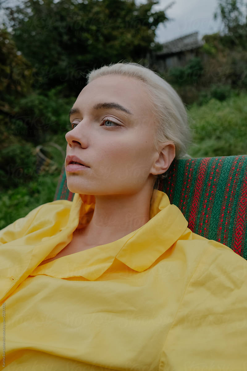 portrait of a stylish girl in a yellow retro dress who sits in a chair in a Russian village