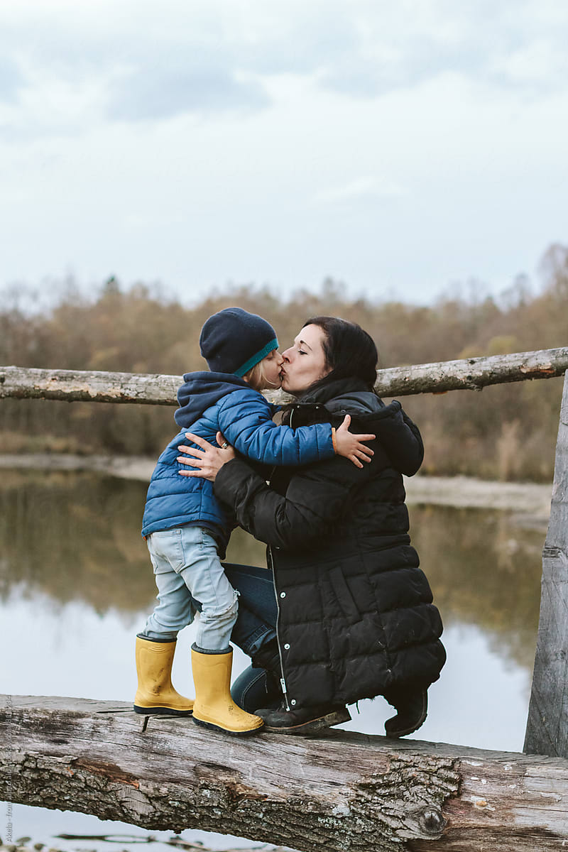 mother and son kissing on a wooden bridge in autumnal landscape