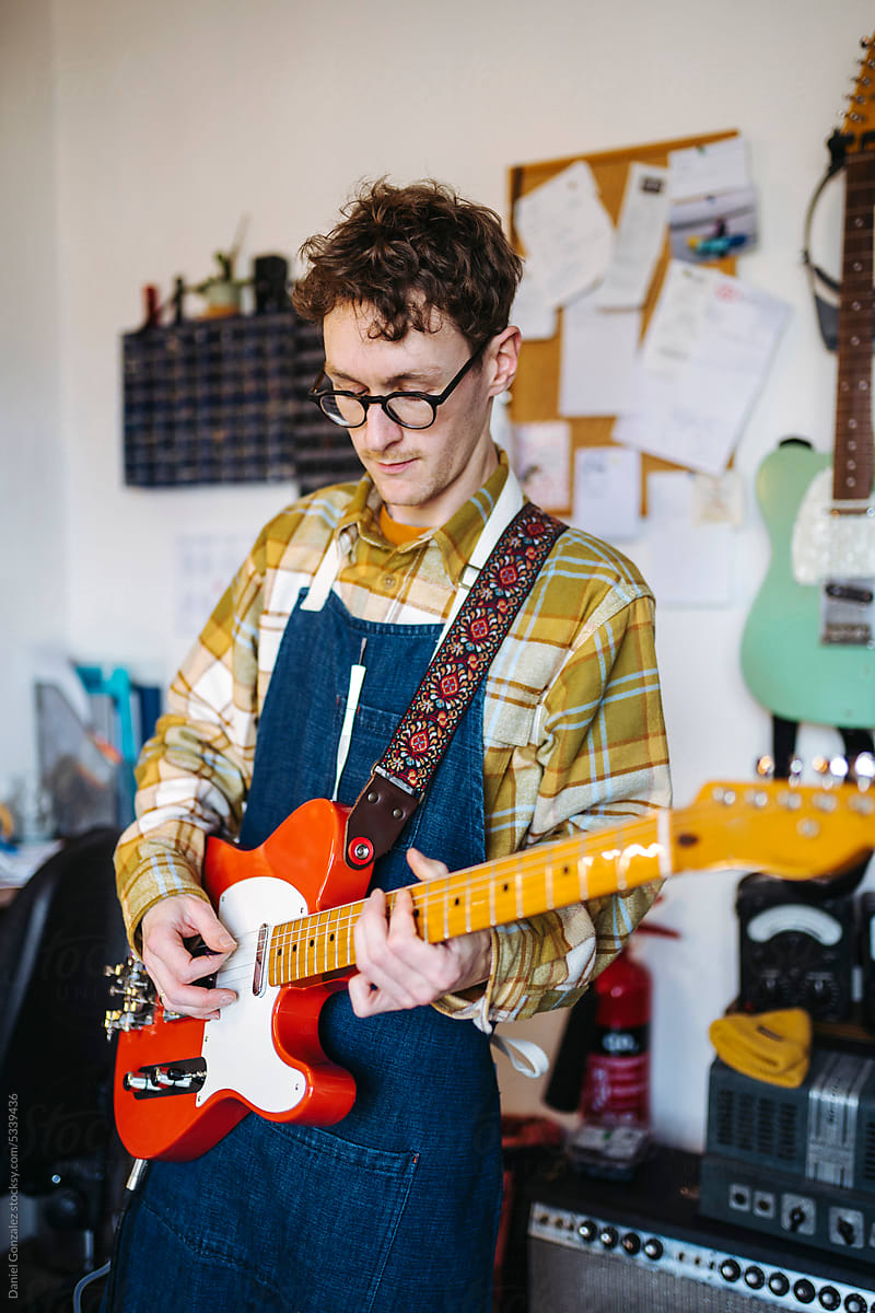 Male musician playing guitar in own repair shop