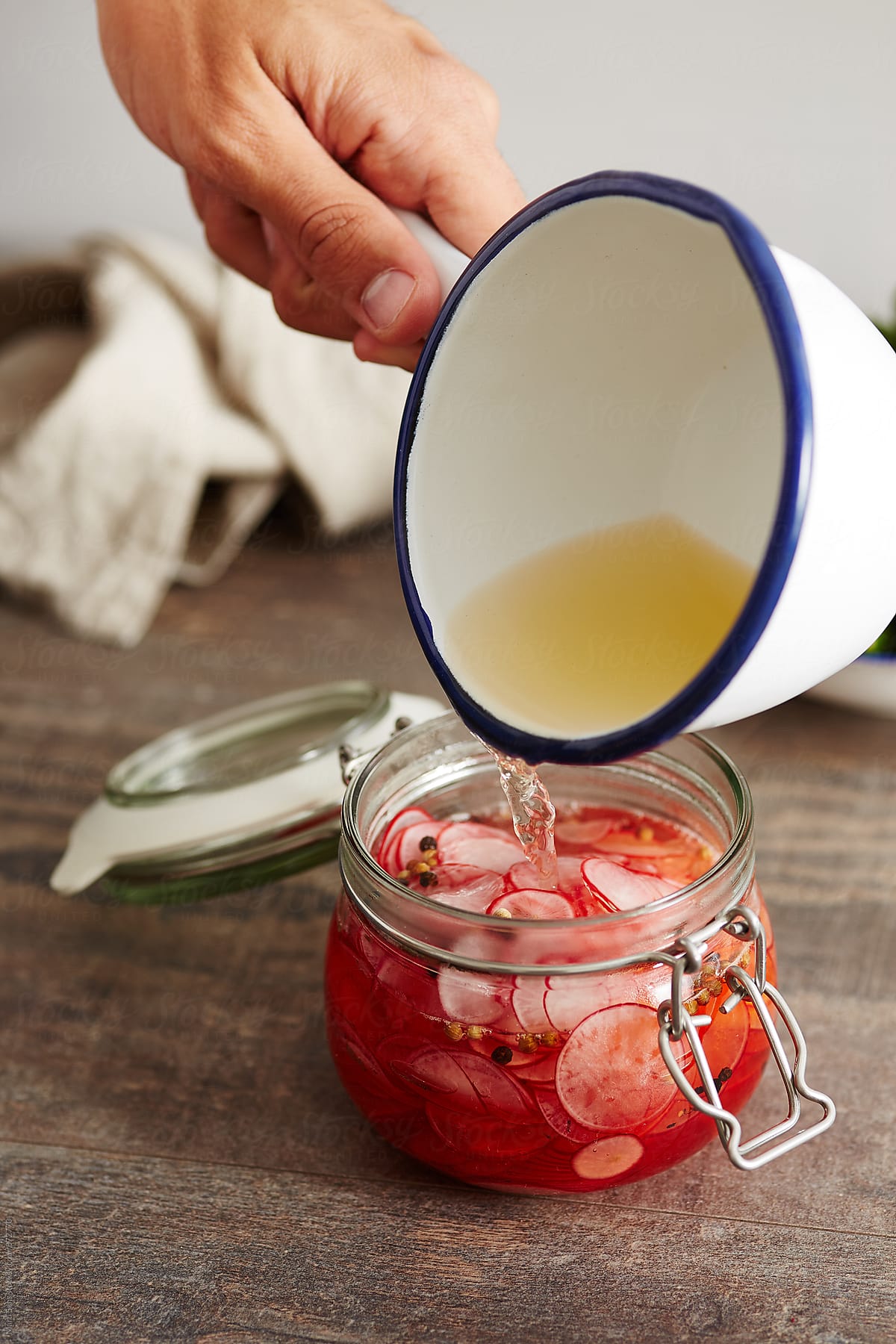 Hand pouring liquid in jar with sliced radish