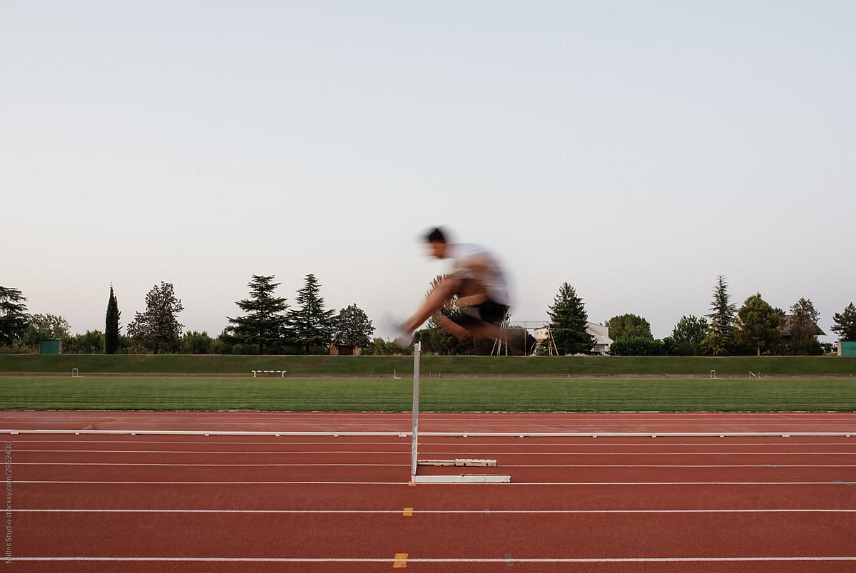 Unrecognizable sportsman leaping over hurdle in evening