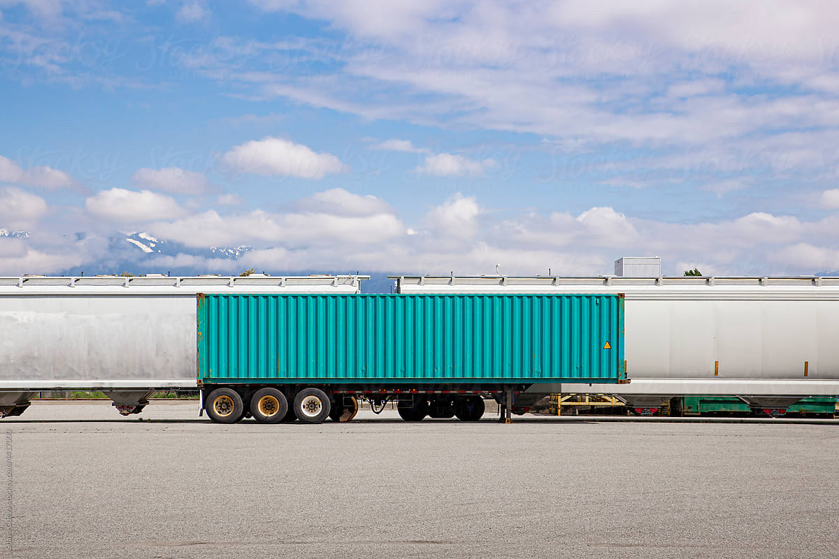 An aqua colored ship container in front of some train cars