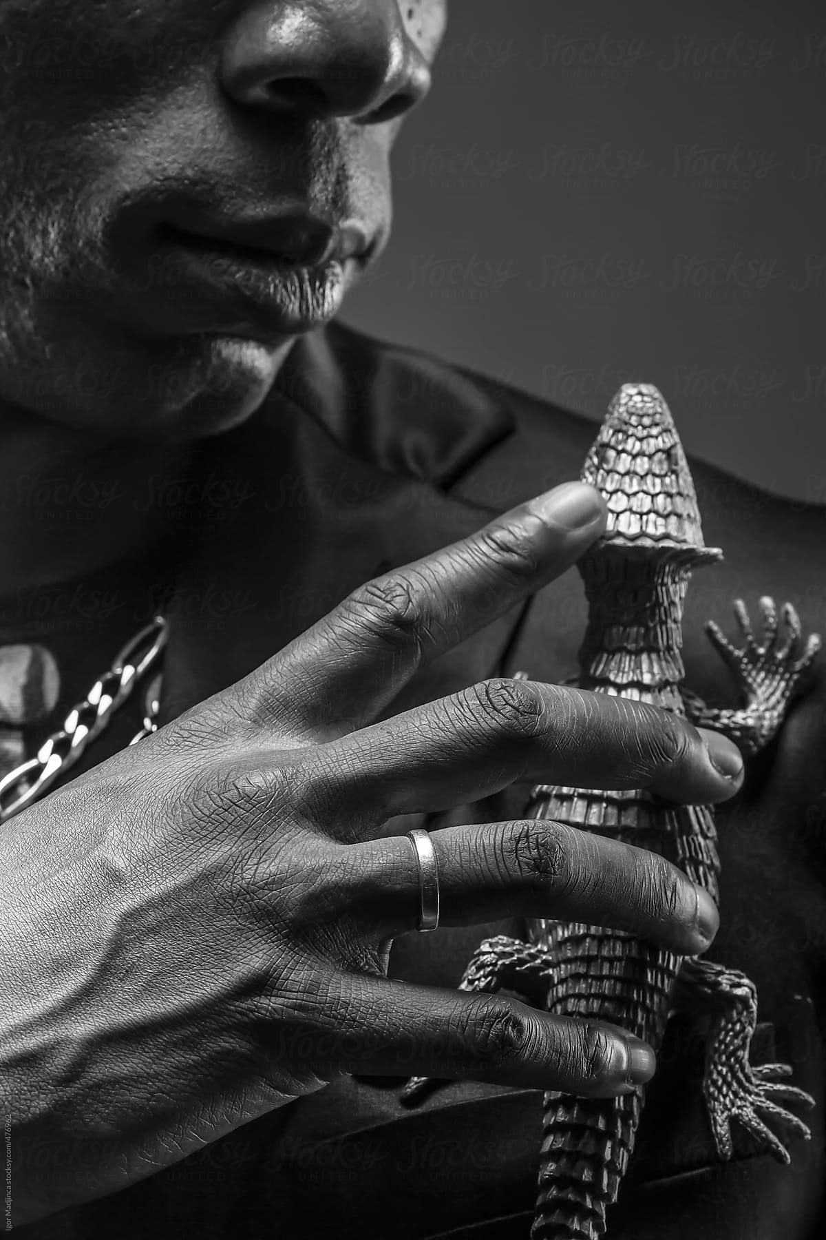 black man with a wedding ring on his hand holding a lizard toy , black and white
